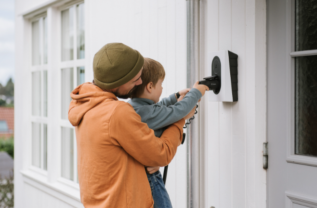 Far og soen saetter ladekabel i Ladestander til elbil